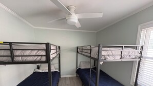 A room with bunk beds, a ceiling fan, and a window with blinds.