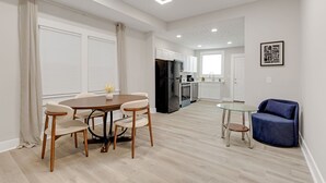 A modern kitchen with white cabinets, a black refrigerator, and a dining area with a round table and chairs. - Cozy Indy Retreat. Walk to Lucas Oil & Downtown. (Indianapolis)