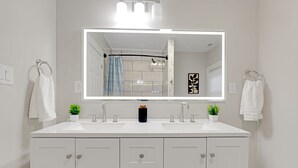 A modern bathroom with a large mirror, two sinks, and a shower curtain. - Cozy Indy Retreat. Walk to Lucas Oil & Downtown. (Indianapolis)