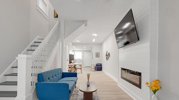 A modern living room with a staircase, a blue sofa, a round coffee table, and a flat-screen TV mounted on the wall. - Cozy Indy Retreat. Walk to Lucas Oil & Downtown. (Indianapolis)