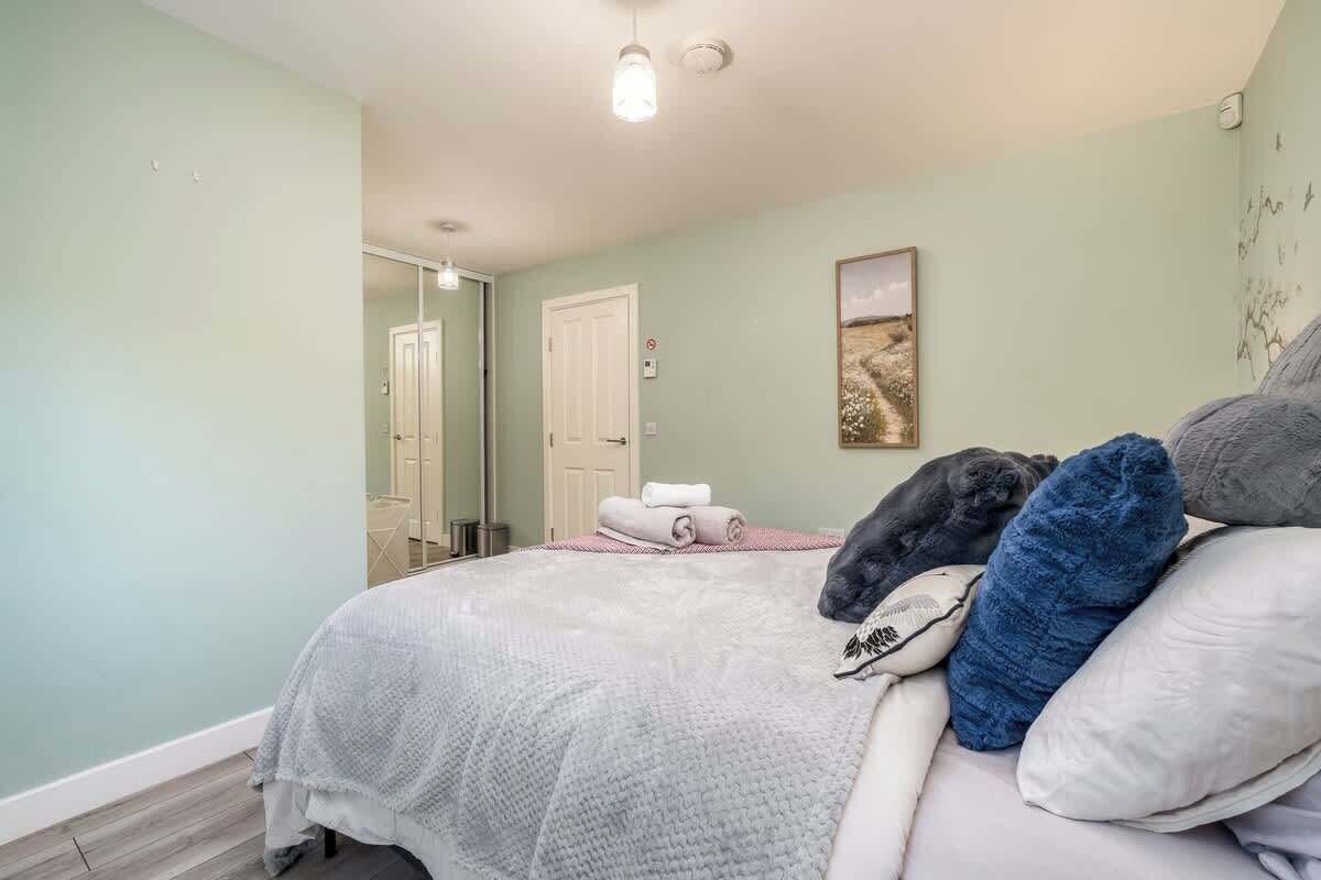 A bedroom with a bed, pillows, a towel, a door, and a painting on the wall.