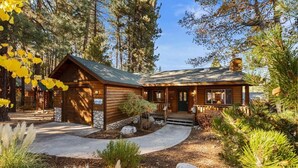 A log cabin with a porch, surrounded by trees and a stone pathway. - Evergreen (Big Bear Lake)