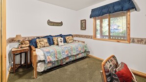 A bedroom with a bed, a nightstand, a chair, a window with blinds, and a wall with a mounted picture frame. - Evergreen (Big Bear Lake)