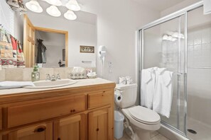 A bathroom with a wooden vanity, a toilet, a shower with glass doors, and a mirror with lights. - Evergreen (Big Bear Lake)