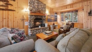 A cozy cabin interior with a stone fireplace, wooden walls, a sofa, and a television. - Evergreen (Big Bear Lake)