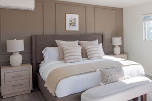 A bedroom with a large bed, two bedside tables with lamps, a bench, and a framed botanical print on the wall. - New Luxury Retreat+Game Room+BBQ+Gym+2 King Suites (Monterey Park)