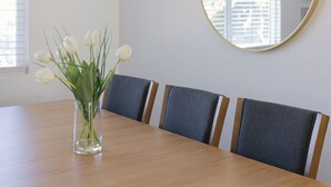 Uma mesa de jantar com um vaso de tulipas brancas, cadeiras estofadas cinzentas e um espelho redondo na parede.