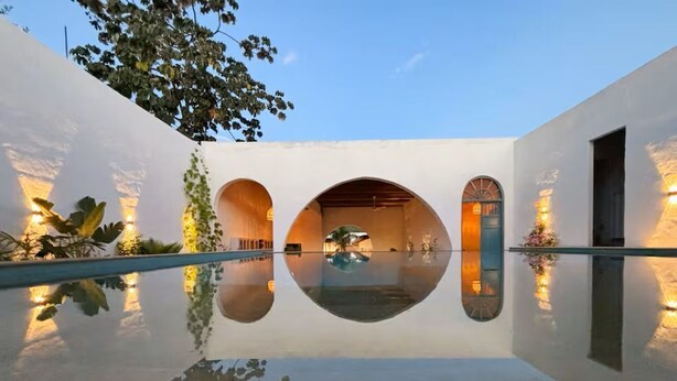 Un edificio moderno con un estanque reflectante, aberturas en arco y luces fijadas a la pared.