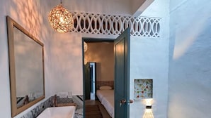 Un baño moderno con un espejo grande, una bañera blanca e iluminación decorativa en el techo.