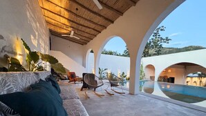 Un área de estar al aire libre con techo, con piscina, que incluye un sofá y sillas, y vistas a la piscina.