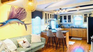 A cozy kitchen with wooden cabinets, a dining area with a green sofa and chairs, and a decorative fish wall art piece. - Spacious 2-Bedroom Coastal Retreat with Luxurious Marble Shower – Beaufort, NC (Beaufort)