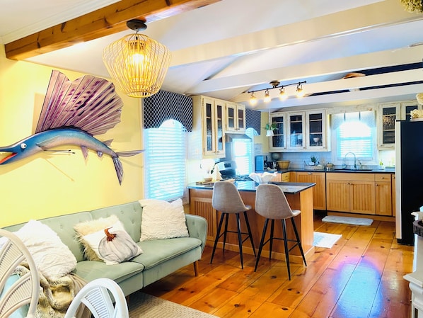 A cozy kitchen with wooden cabinets, a dining area with a green sofa and chairs, and a decorative fish wall art piece.