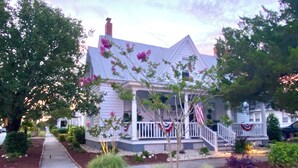 A two-story house with a porch, a small garden, and a flag. - Spacious 2-Bedroom Coastal Retreat with Luxurious Marble Shower – Beaufort, NC (Beaufort)