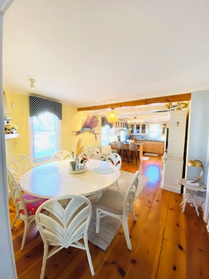 A dining area with a round table, white chairs, and a kitchen in the background.