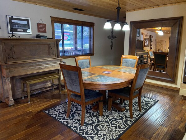 A dining area with a round wooden table, four chairs, a piano, and a patterned rug. - Alpine Summit Lodge - Formally 4K Penthouse View (Red River)