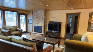 Ein Wohnzimmer mit Ledersofas, einem Steinkamin, einem Fernseher und Holzbalken an der Decke.