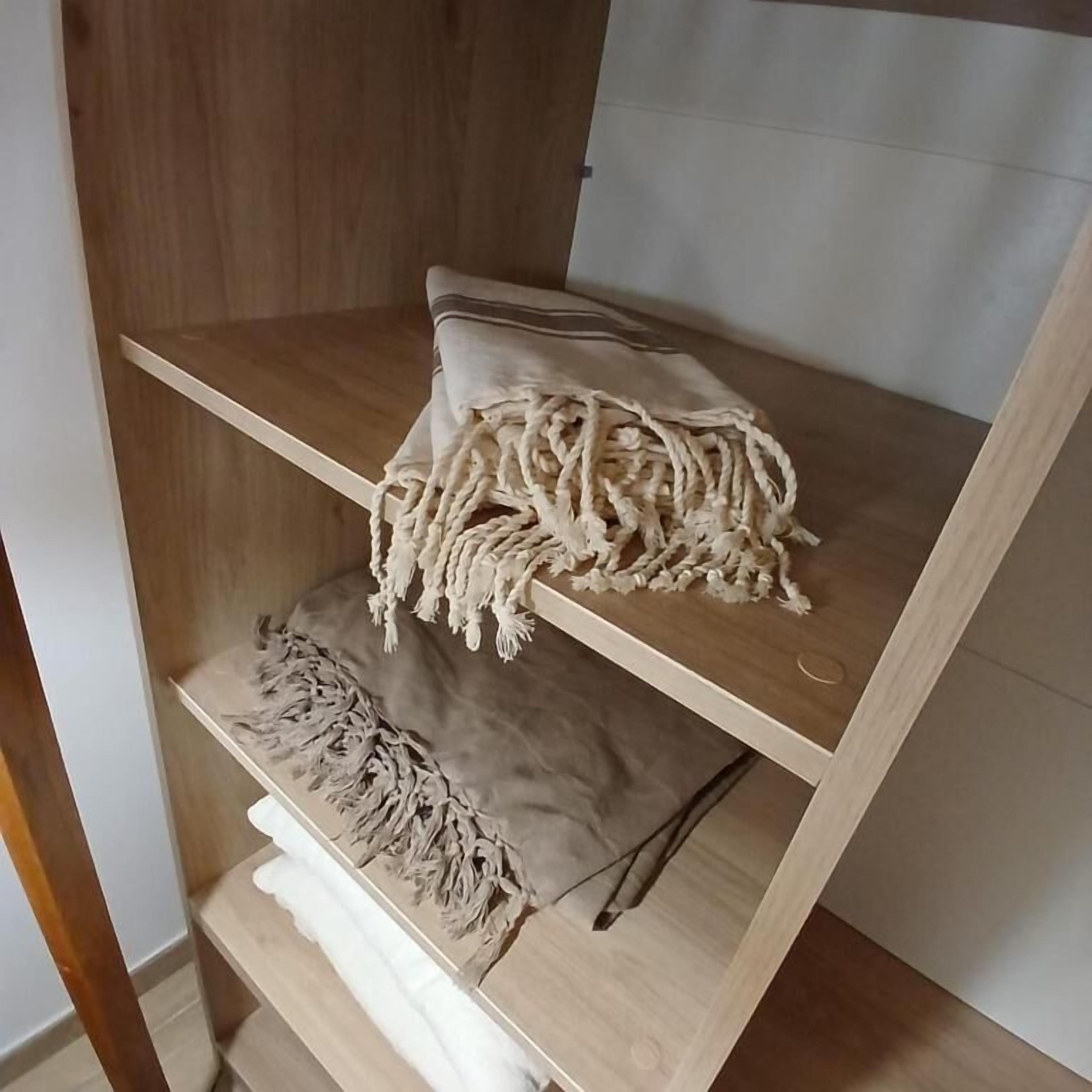 Une étagère en bois avec un coussin beige et une pièce en macramé.