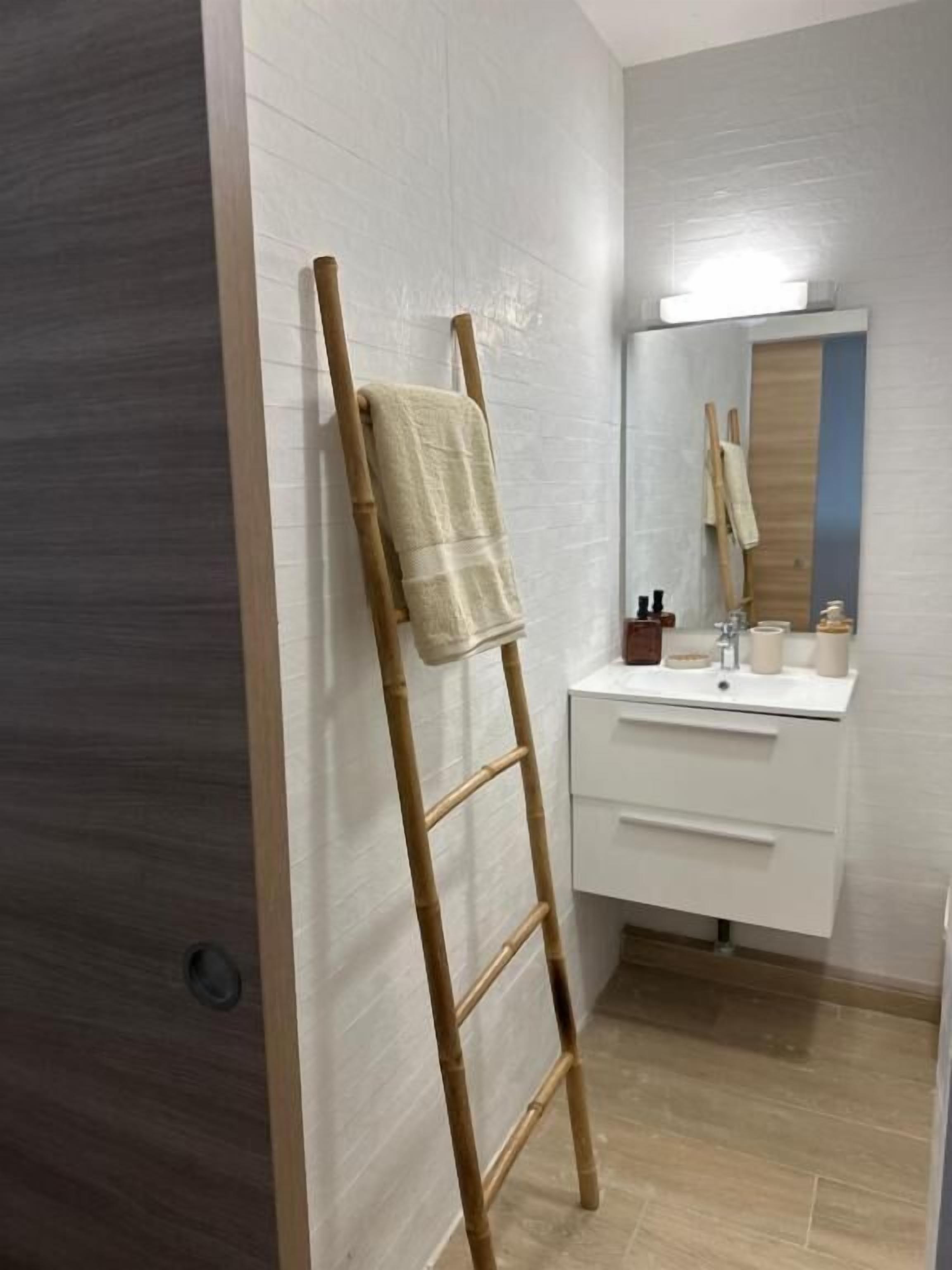 Une salle de bain avec une échelle en bois appuyée contre le mur, un lavabo avec des articles de toilette et un miroir au-dessus du lavabo.