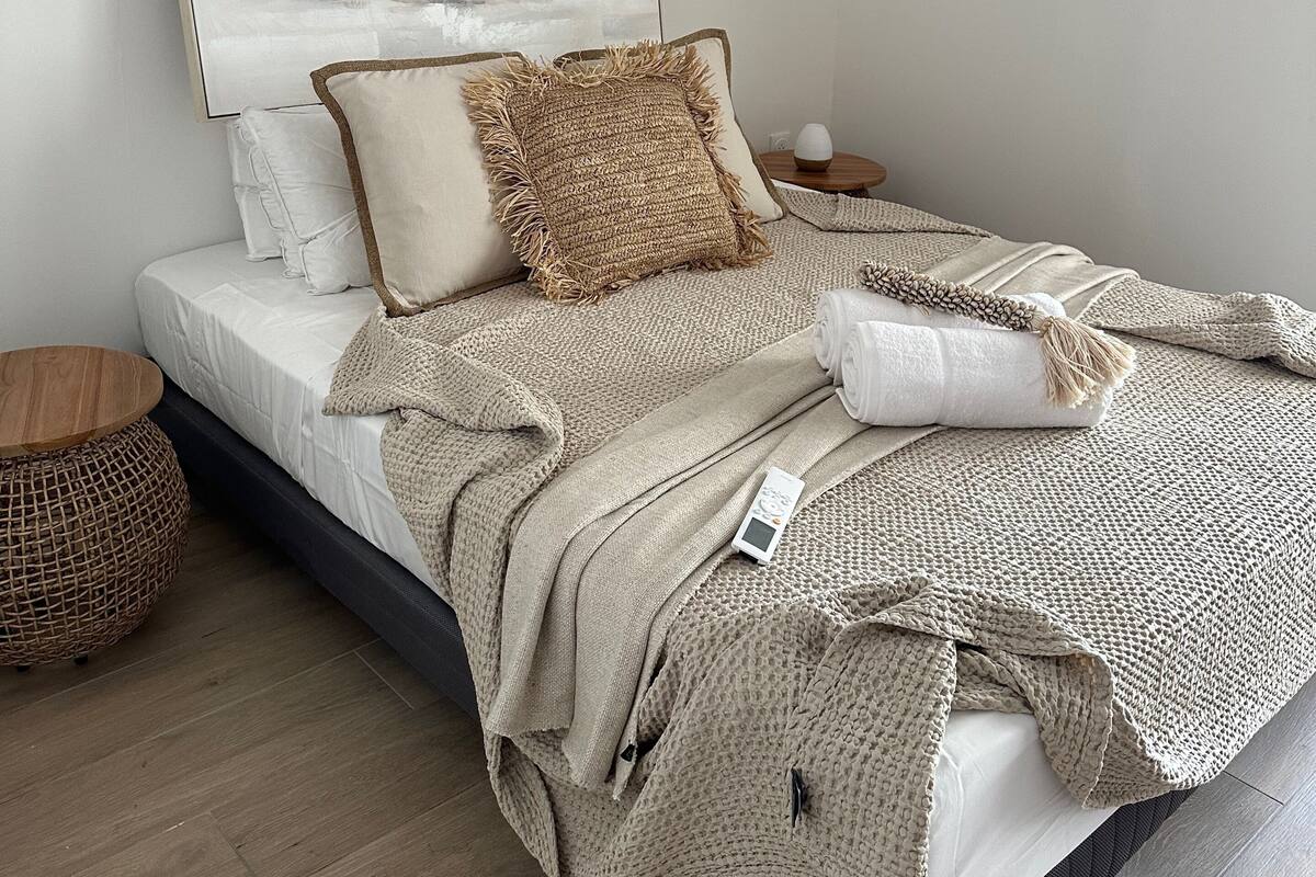 Un lit bien fait, avec une couette blanche, un plaid tricoté beige et un oreiller.