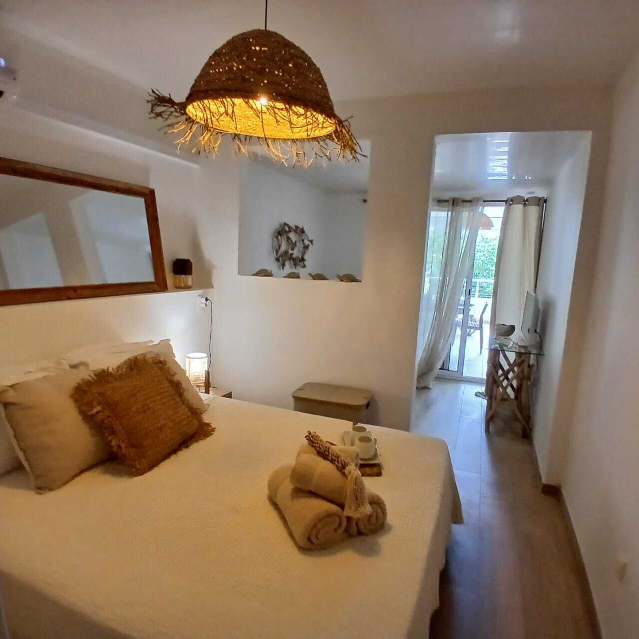 A bedroom with a bed, a bedside table, a mirror, and a view of a balcony.