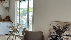 Ein modernes Wohnzimmer mit Sofa, Esstisch mit Stühlen, Küchenzeile und einem großen Fenster mit Blick.
