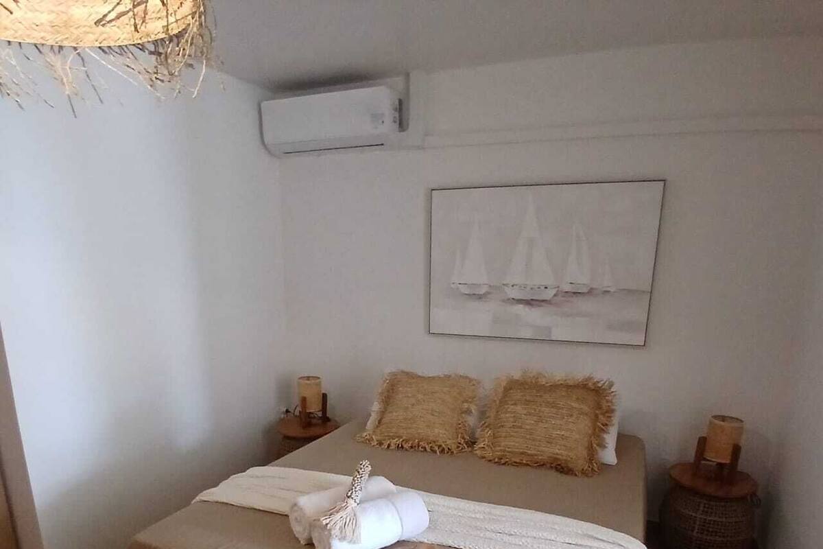 Une chambre à coucher avec un lit, un climatiseur fixé au mur, un tableau encadré et une table de chevet avec une bougie.