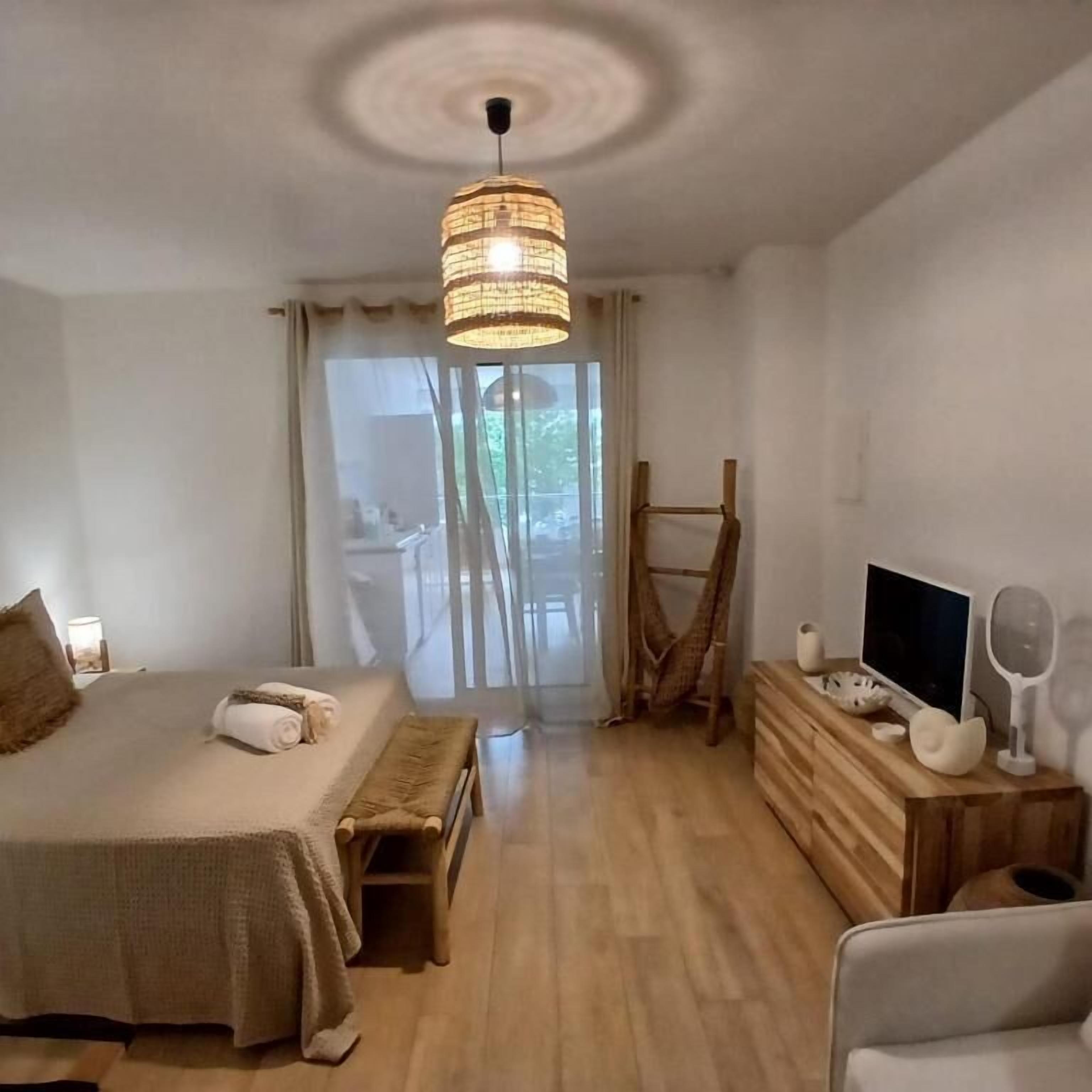 Un dormitorio con cama, mesita de noche, televisión y vistas al exterior.