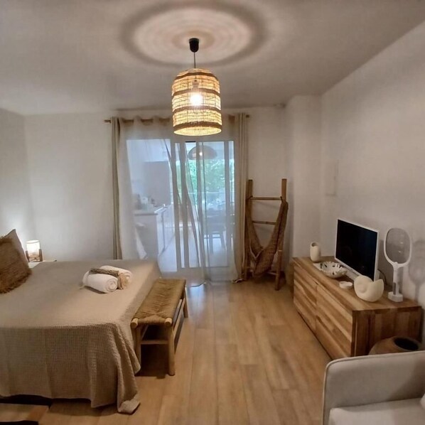 A bedroom with a bed, bedside table, TV, and a view of the outdoors.