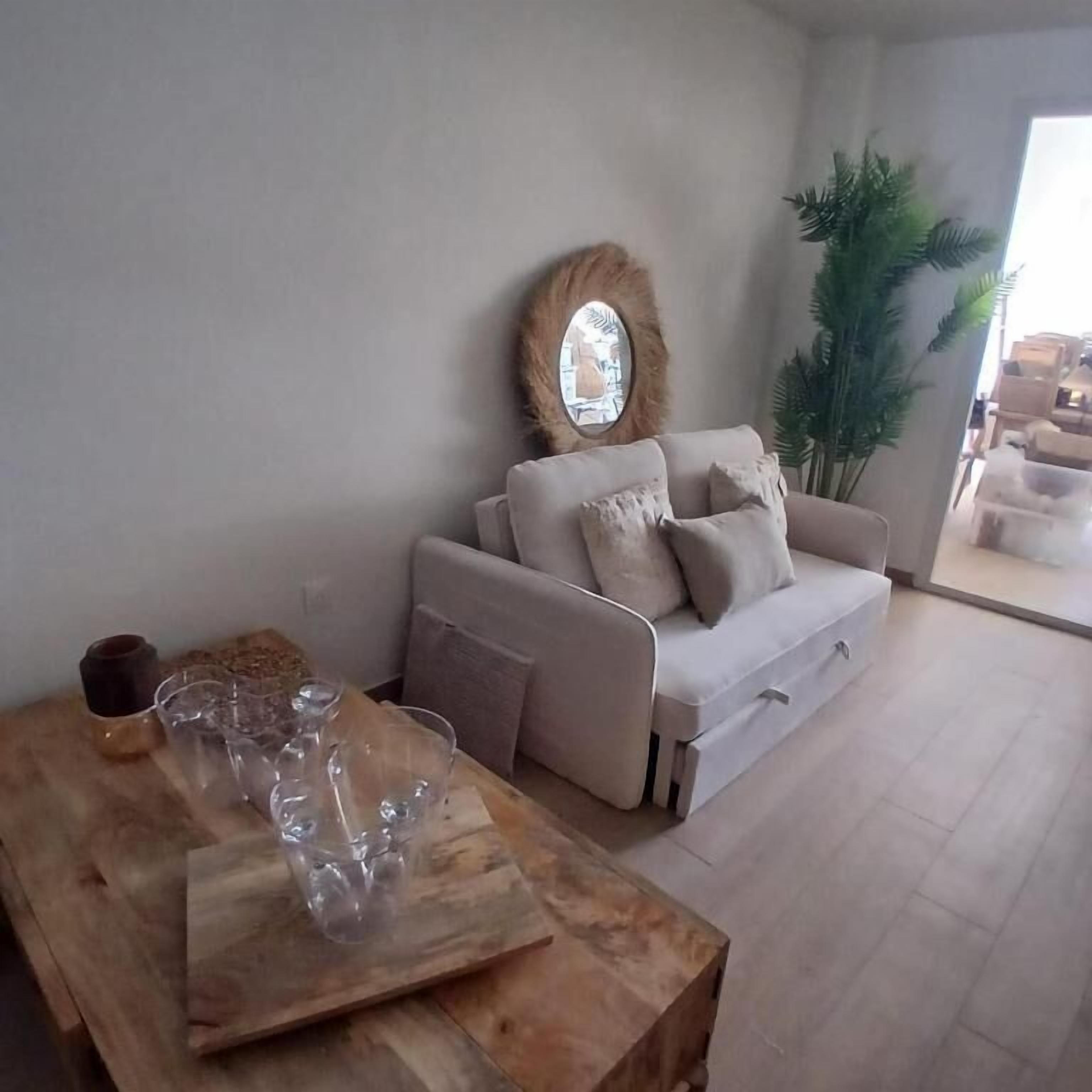 Una sala de estar con un sofá, una mesa de centro con vasos, un espejo redondo y una planta en maceta.