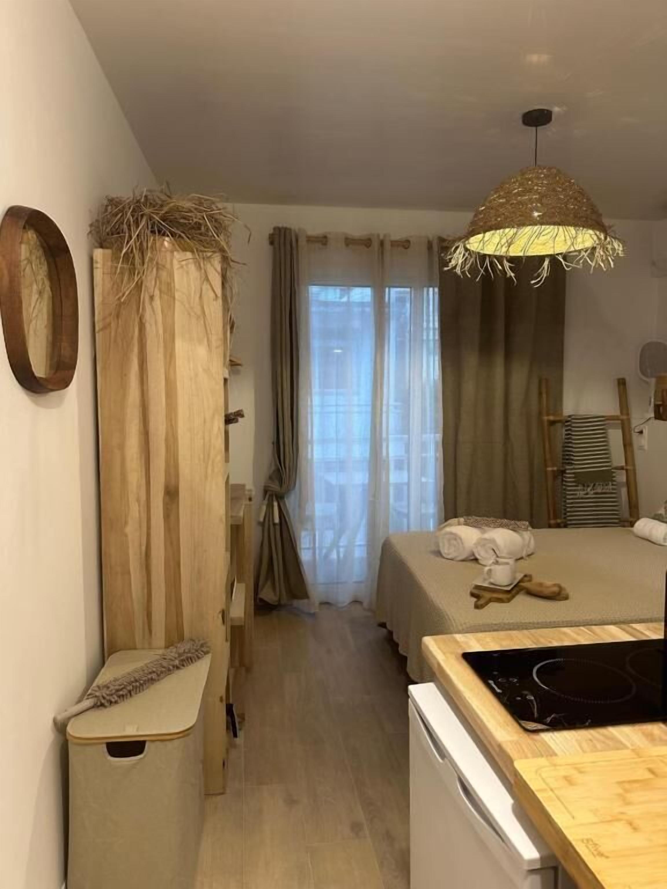 A room with a bed, a wooden cabinet, a small table, a ceiling light fixture, and a window with curtains.