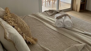 Ein Schlafzimmer mit Bett, einem großen Fenster und Blick auf einen Außenbereich mit Essplatz.
