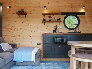 Une chambre confortable, aménagée dans le style d’un chalet, avec un canapé, une table ronde, une kitchenette équipée d’un four à micro-ondes et une fenêtre donnant sur un paysage verdoyant.