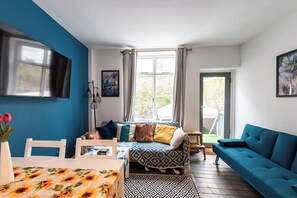 Een kamer met een bed, een blauwe bank, een televisie en een raam met gordijnen.