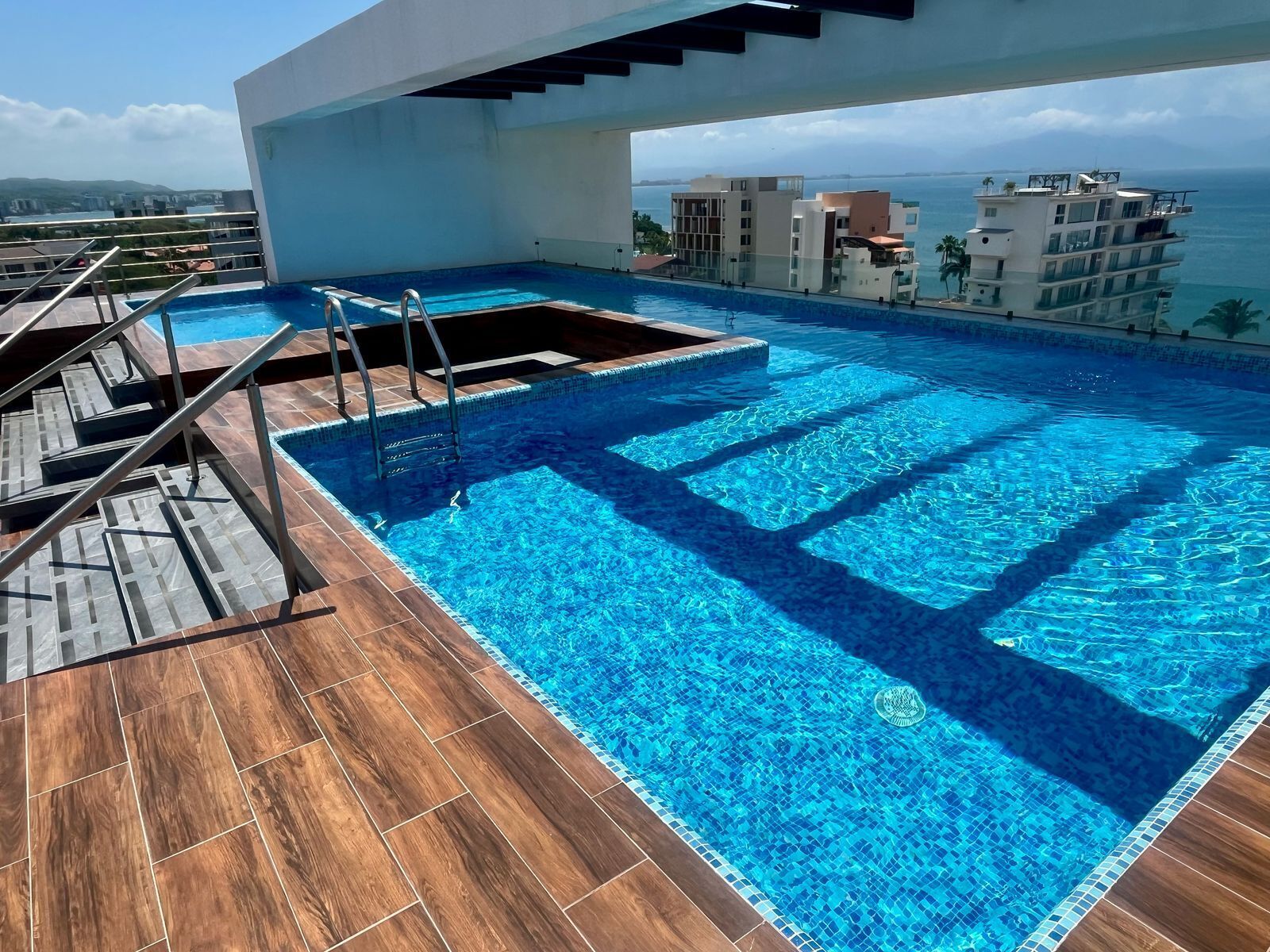 Una piscina infinita en la azotea con cubierta de madera y vista al mar.