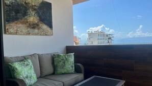A balcony with a sofa and a glass table, a painting on the wall, and a view of buildings and the sky. - Department La Cruz de Huanacaxtle, Nayarit. With two bedrooms with bathroom (Cruz de Huanacaxtle)