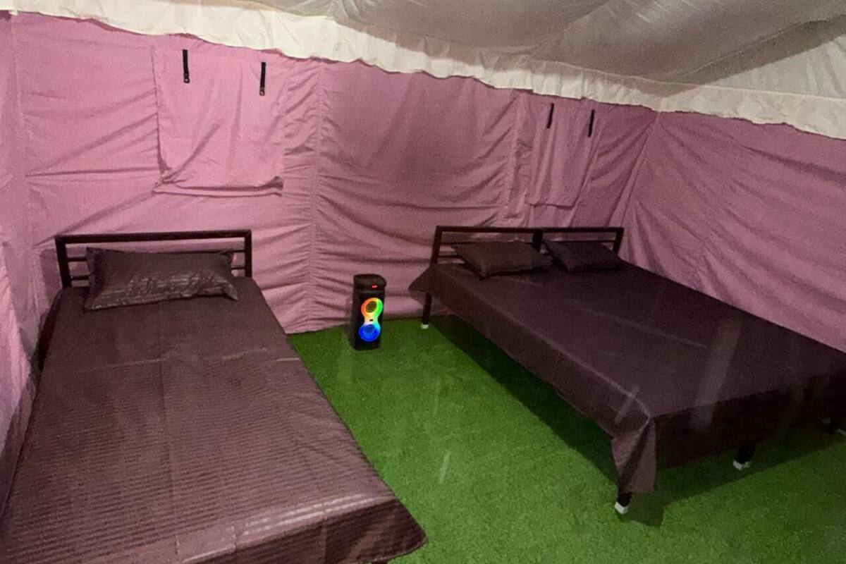 Una habitación tipo tienda de campaña con dos camas, una mesita pequeña y un objeto de colores en el suelo.