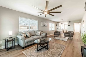 A modern living room with a sofa, coffee table, and chairs, a ceiling fan, and a kitchen in the background. - Waterfront Modern and Spacious Condo 2 Bed/2bath (Clearwater)