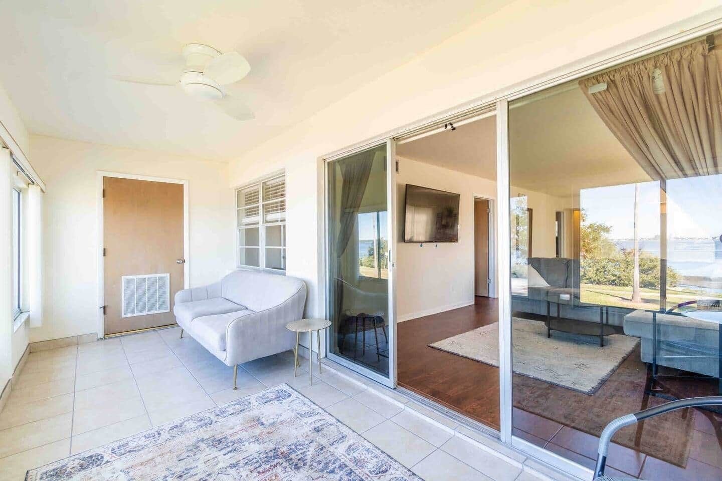 A modern living room with a sofa, a small table, and a large sliding glass door leading to a balcony.