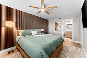 A bedroom with a bed, wooden panel wall, ceiling fan, and a bathroom with a toilet and sink. - Beautiful waterfront 2 bedroom condo (Clearwater)