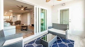 Ein modernes Wohnzimmer mit Glastür zum Balkon, Deckenventilator und Essbereich mit Tisch und Stühlen.