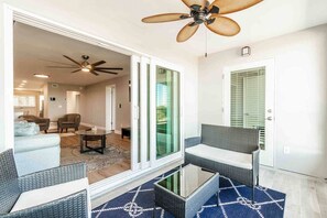 A modern living room with a glass door leading to a balcony, a ceiling fan, and a dining area with a table and chairs. - Waterfront Updated Coastal Condo 2 Bed/2 bath (Clearwater)