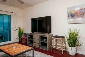 A living room with a TV, wooden entertainment unit, a small stool, and a potted plant. - Waterfront Condo in Dunedin/Clearwater (Clearwater)
