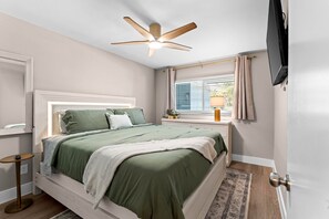 A bedroom with a bed, a bedside table, a ceiling fan, a window with curtains, and a television on the wall. - Waterfront Condo in Dunedin/Clearwater (Clearwater)