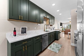 A modern kitchen with dark green cabinets, a marble countertop, and a view to the dining area. - Waterfront Condo in Dunedin/Clearwater (Clearwater)