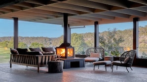 A covered outdoor seating area with a wood-burning stove, a sofa, and chairs, overlooking a scenic landscape. - Grants - spacious riverside escape on the Shoalhaven River (Longreach)