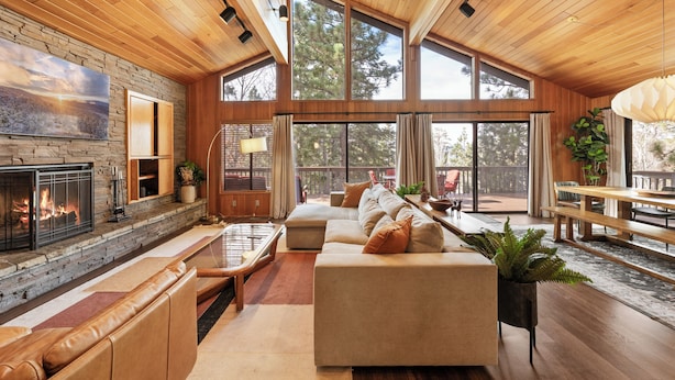 A spacious living area with a fireplace, large windows, a sofa, and a dining table. - Modern Primrose (Big Bear Lake)