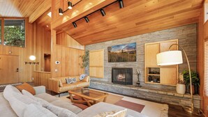 A spacious living room with a stone fireplace, wooden ceiling, and a large sofa. - Modern Primrose (Big Bear Lake)