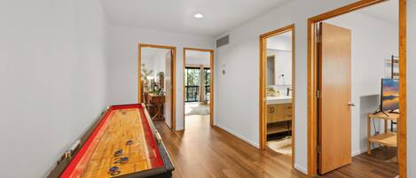 A hallway with a pool table, wooden flooring, and open doors leading to other rooms.