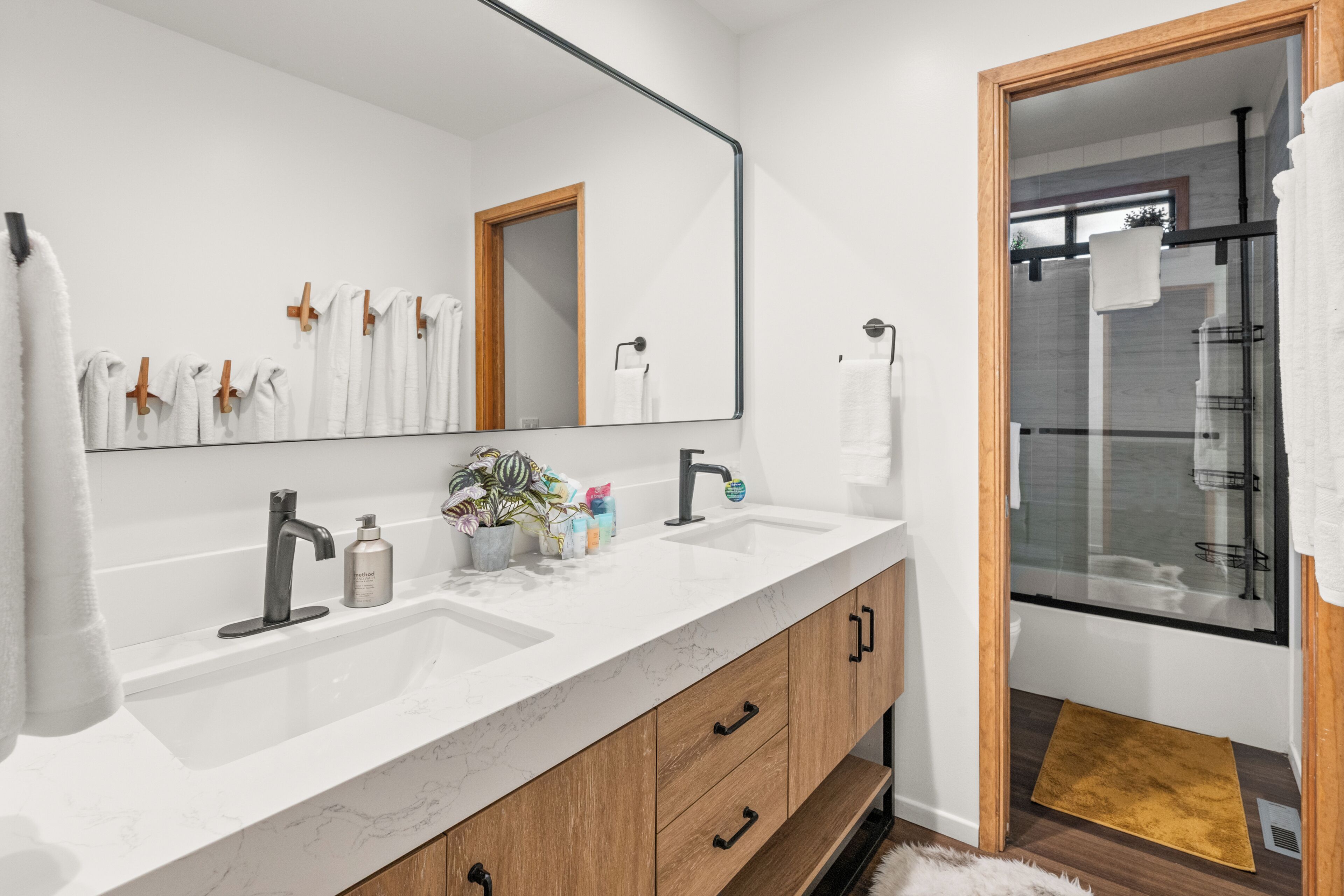 Un baño moderno con un espejo grande, dos lavamanos, armarios de madera y una zona de ducha.
