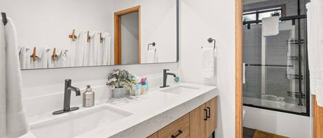 Un baño moderno con un espejo grande, dos lavamanos, armarios de madera y una zona de ducha.